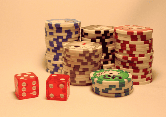 Stacks of colorful casino chips and two red dice on a neutral background, representing gambling rewards and the question How Do Casino Bonuses Work.